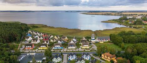 An aerial view of a lakeside village with houses, a lighthouse, and a large body of water.