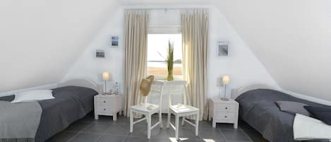 Un dormitorio con dos camas, una mesita y una silla. Hay dos mesitas de noche con lámparas, una ventana con cortinas y vistas al exterior.