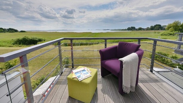 Un balcon avec un canapé violet et un pouf jaune, donnant sur un champ verdoyant.