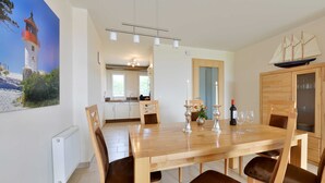 Un coin repas avec une table et des chaises en bois, donnant sur la cuisine, et un modèle de bateau accroché au mur.