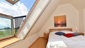 Une chambre avec une lucarne, un lit avec des oreillers, une table de chevet et un tableau au mur.