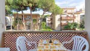 A balcony with a table set for two, overlooking a residential area with apartment buildings and trees. - Lovely apartment in Rosolina Mare (RO) (Rosolina Mare (RO))
