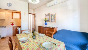 A dining area with a table set for two, a blue sofa, and a kitchen in the background. - Lovely apartment in Rosolina Mare (RO) (Rosolina Mare (RO))