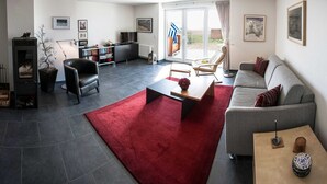A modern living room with a fireplace, a sofa, a coffee table, and a dining area. - Deichhaus Brisinga, Germany (Breege)