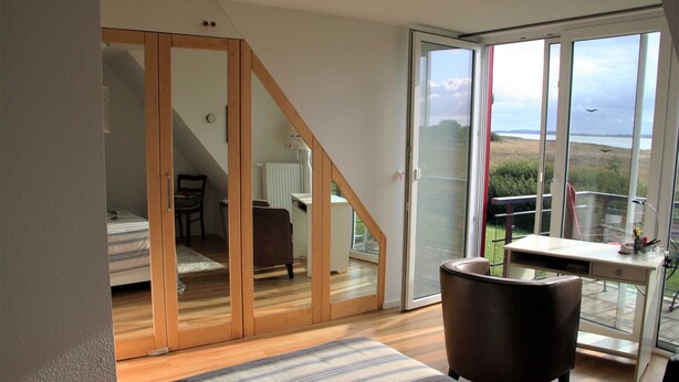A bedroom with a bed, a chair, a desk, and a view of the outdoors through a sliding glass door. - Deichhaus Brisinga, Germany (Breege)