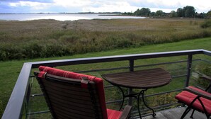 A balcony with a table and two chairs, overlooking a grassy area and a body of water. - Deichhaus Brisinga, Germany (Breege)