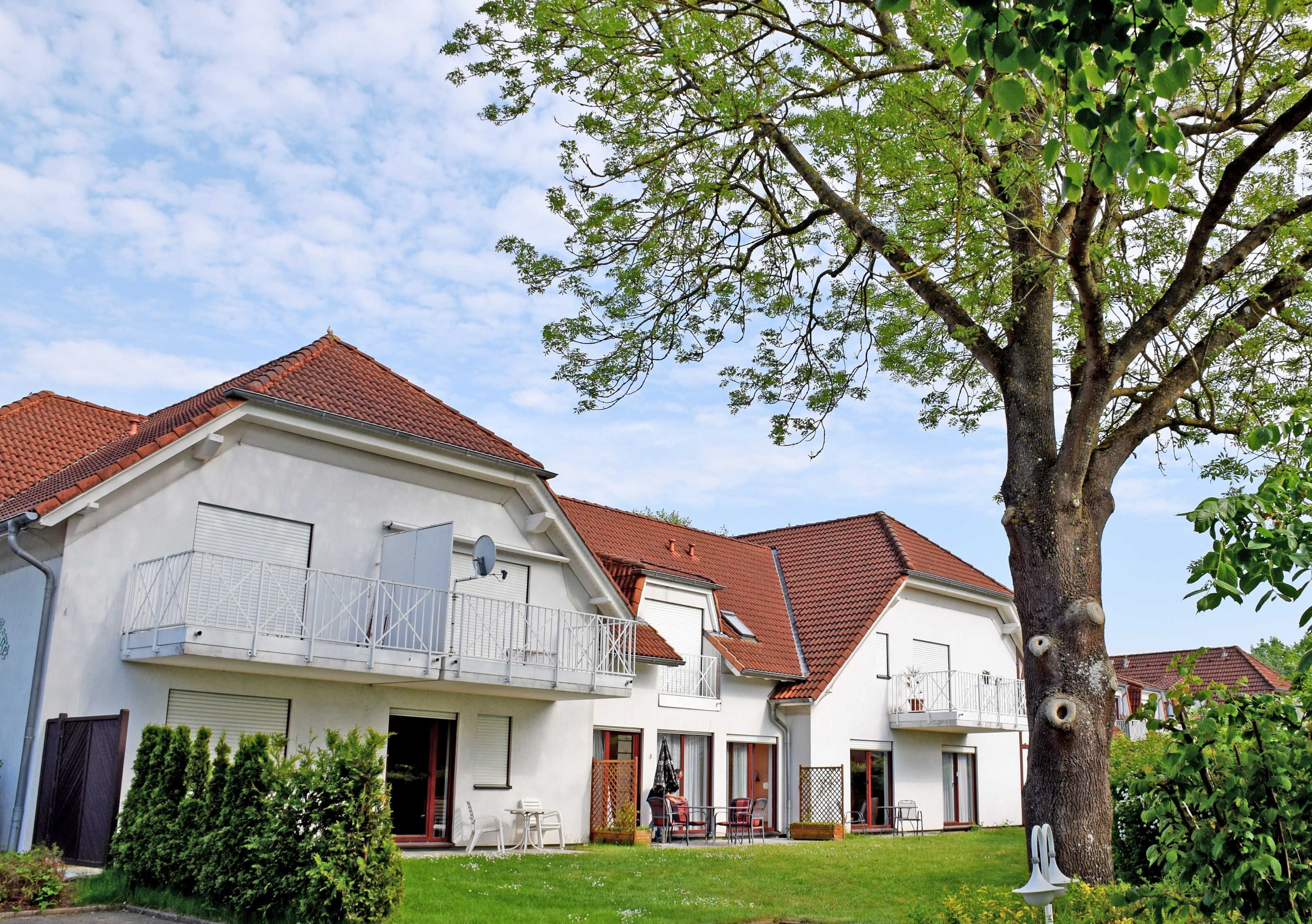 A two-story residential building with a red-tiled roof, a balcony with a white railing, and a well-maintained lawn.