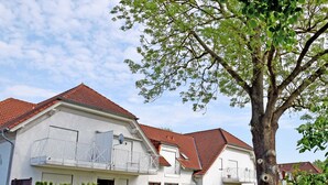 A two-story residential building with a red-tiled roof, a balcony with a white railing, and a well-maintained lawn. - Vacation apartment Victoria with terrace and garden view - Holiday apartment Victoria with (Gustow)