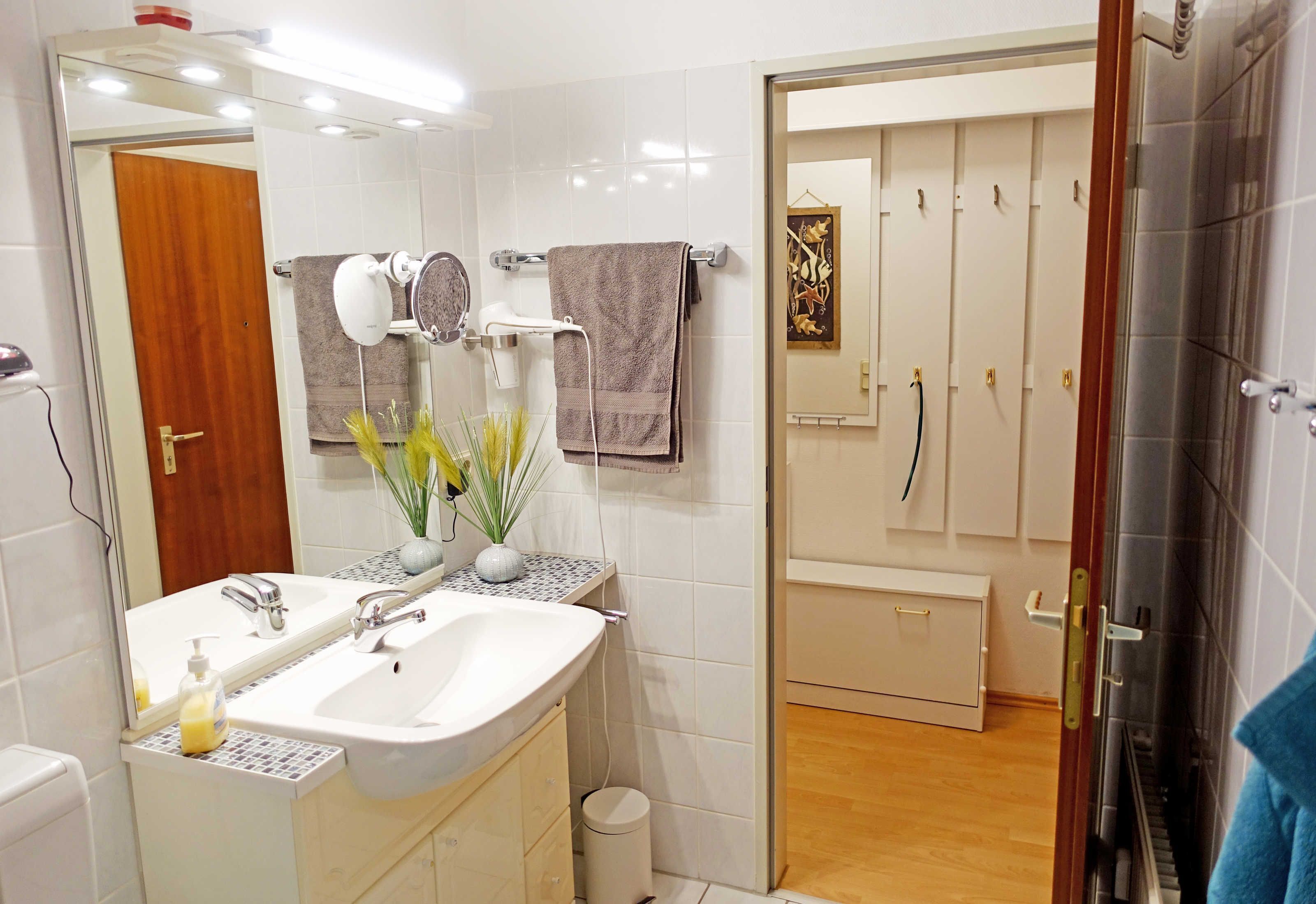 A bathroom with a white sink, mirror, and towel rack. There is a small trash can and a plant on the counter.