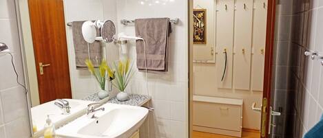 A bathroom with a white sink, mirror, and towel rack. There is a small trash can and a plant on the counter.