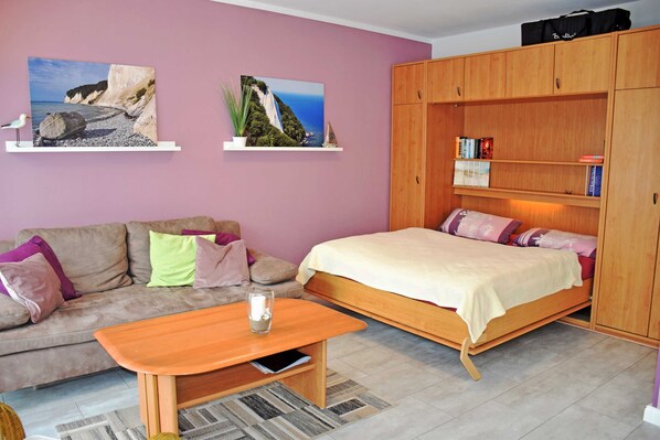 Une chambre à coucher comprenant un lit, un canapé, une armoire en bois et deux étagères murales ornées de livres et d’objets décoratifs.