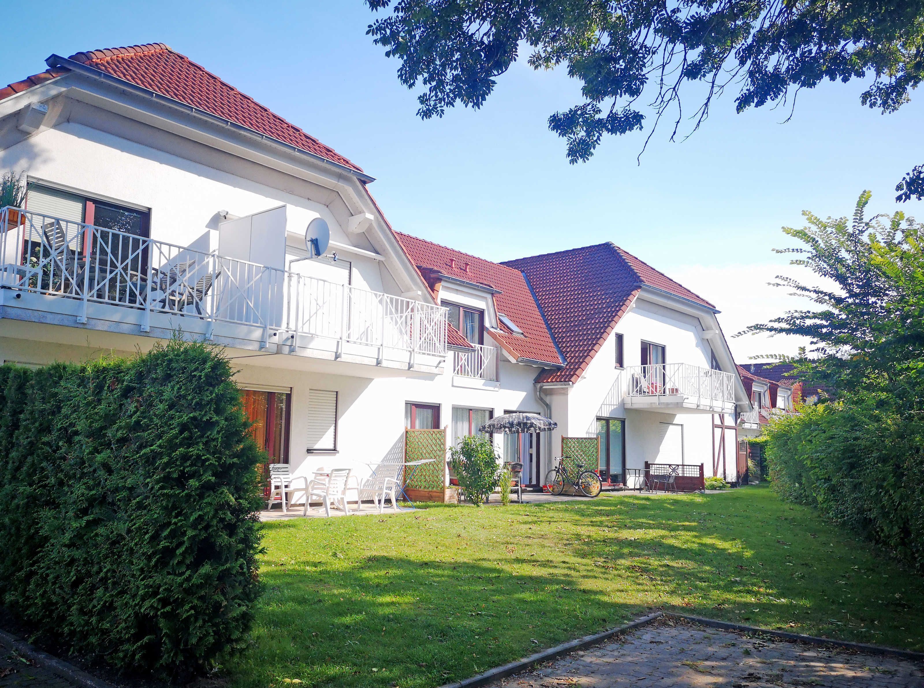 A two-story house with a red-tiled roof, white exterior walls, and a balcony with white railings.