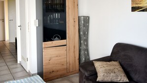 Ett vardagsrum med en mörkbrun soffa, ett träskåp med glasdörrar, en väggdekoration med mönster och en inramad tavla på väggen.