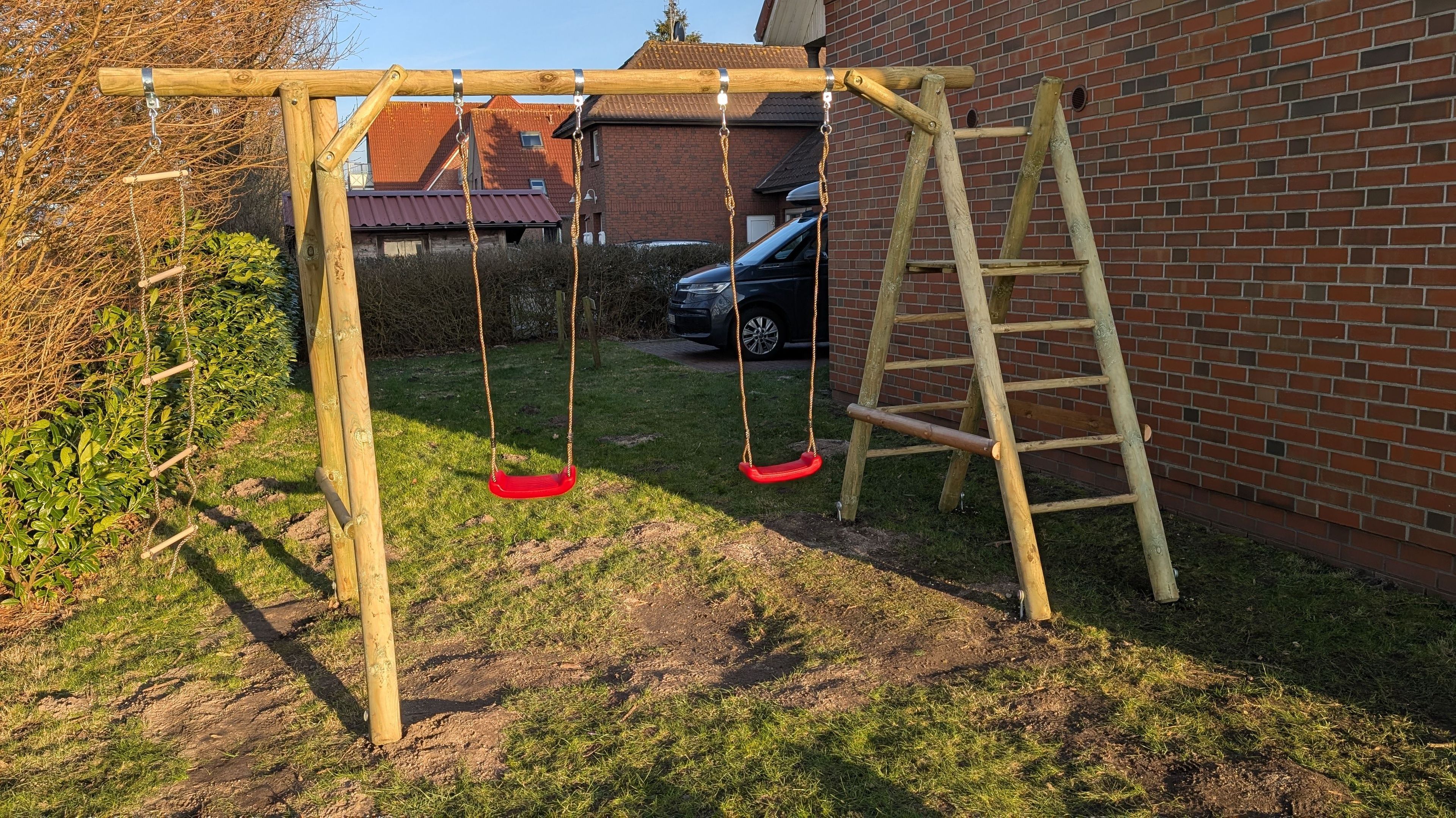 Ein Schaukelgerüst aus Holz mit zwei Schaukeln und einer Kletterleiter in einem Garten.