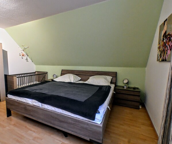 A bedroom with a wooden bed, two bedside tables, a nightstand, and a wall-mounted shelf.