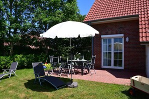 A patio with a table and chairs, a white umbrella, and a brick building with a red roof.