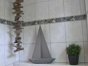A tiled wall with a decorative border, a stone wall art piece, and a potted plant. - Holiday house Carolinenwind (Wittmund)