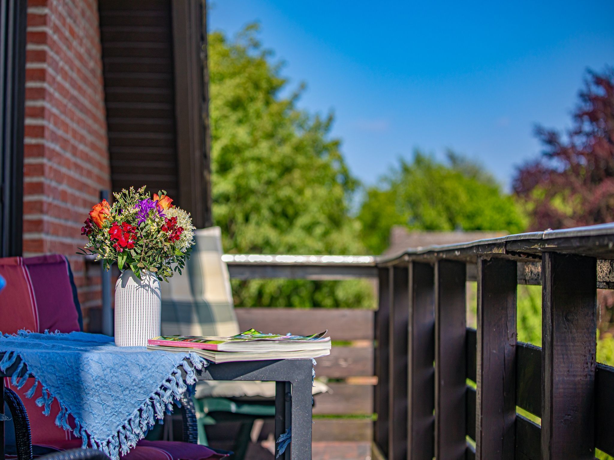 A table with a vase of flowers, a magazine, and a blue cloth on a balcony.