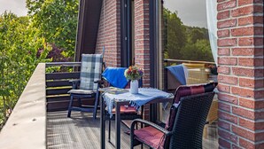 Een terras met rieten meubels, een tafel met een blauwe tafelkleed en een vaas met bloemen.