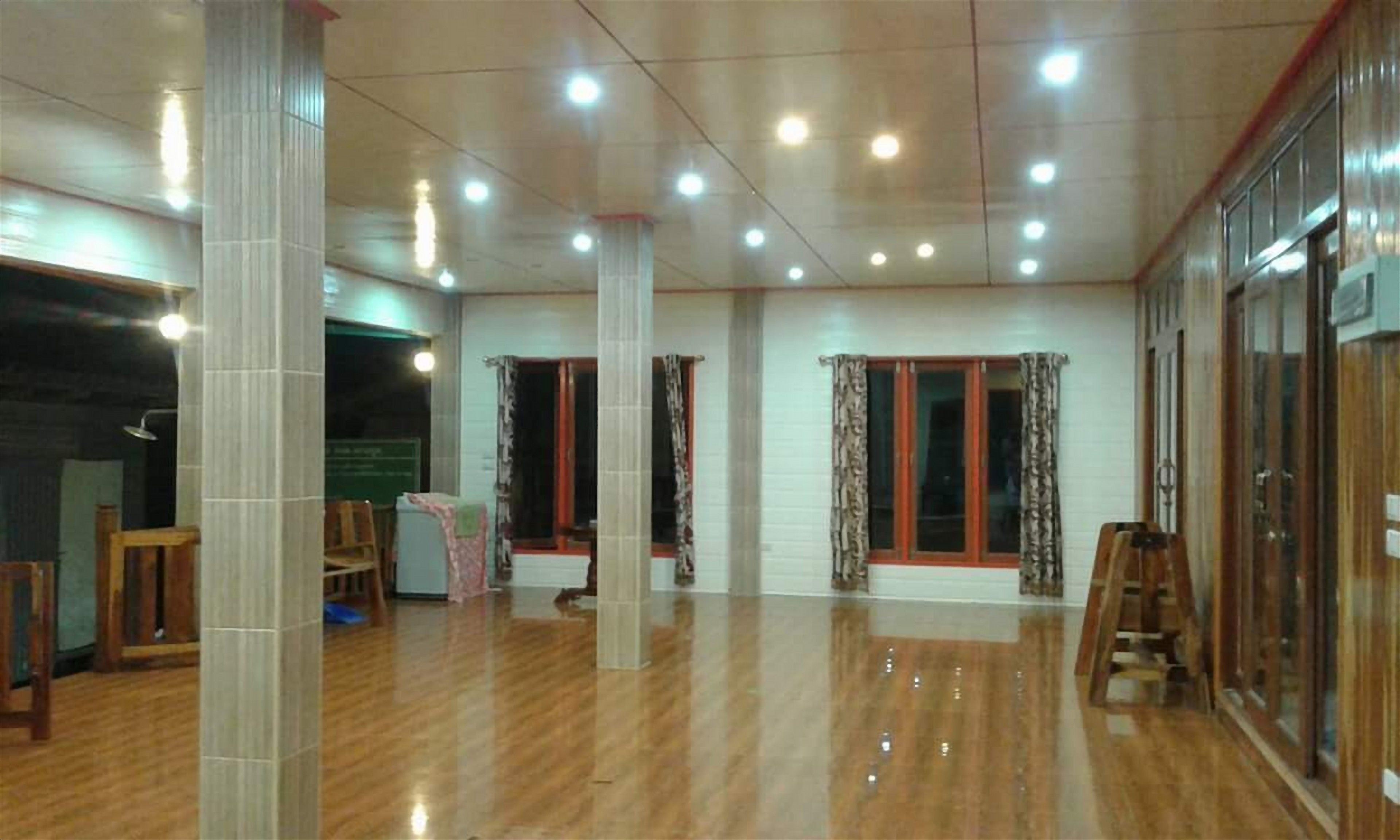 Una habitación amplia con piso de madera pulida, ventanas grandes con cortinas y una escalera de madera.