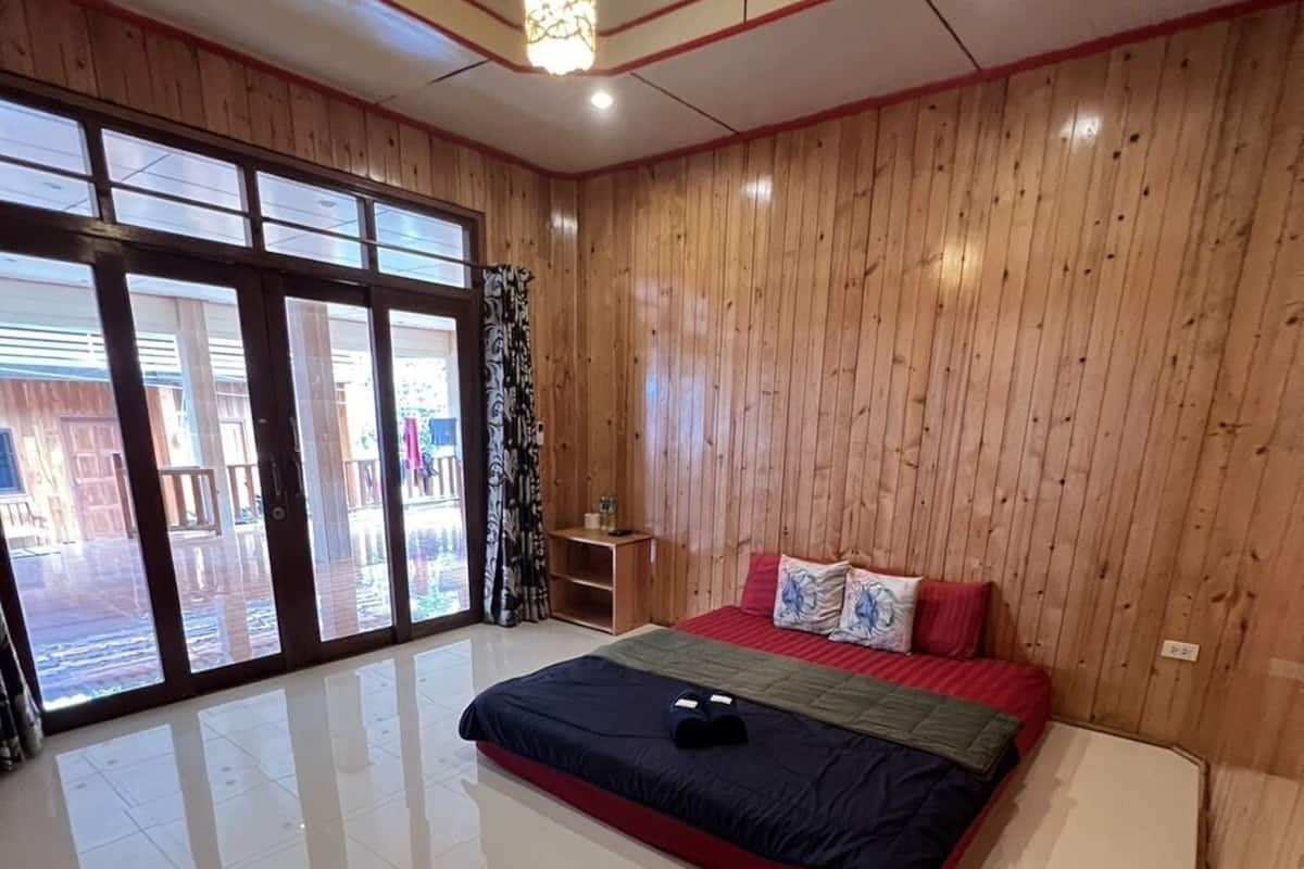 A modern bedroom with a large bed, wooden paneling, and a view through the glass doors.