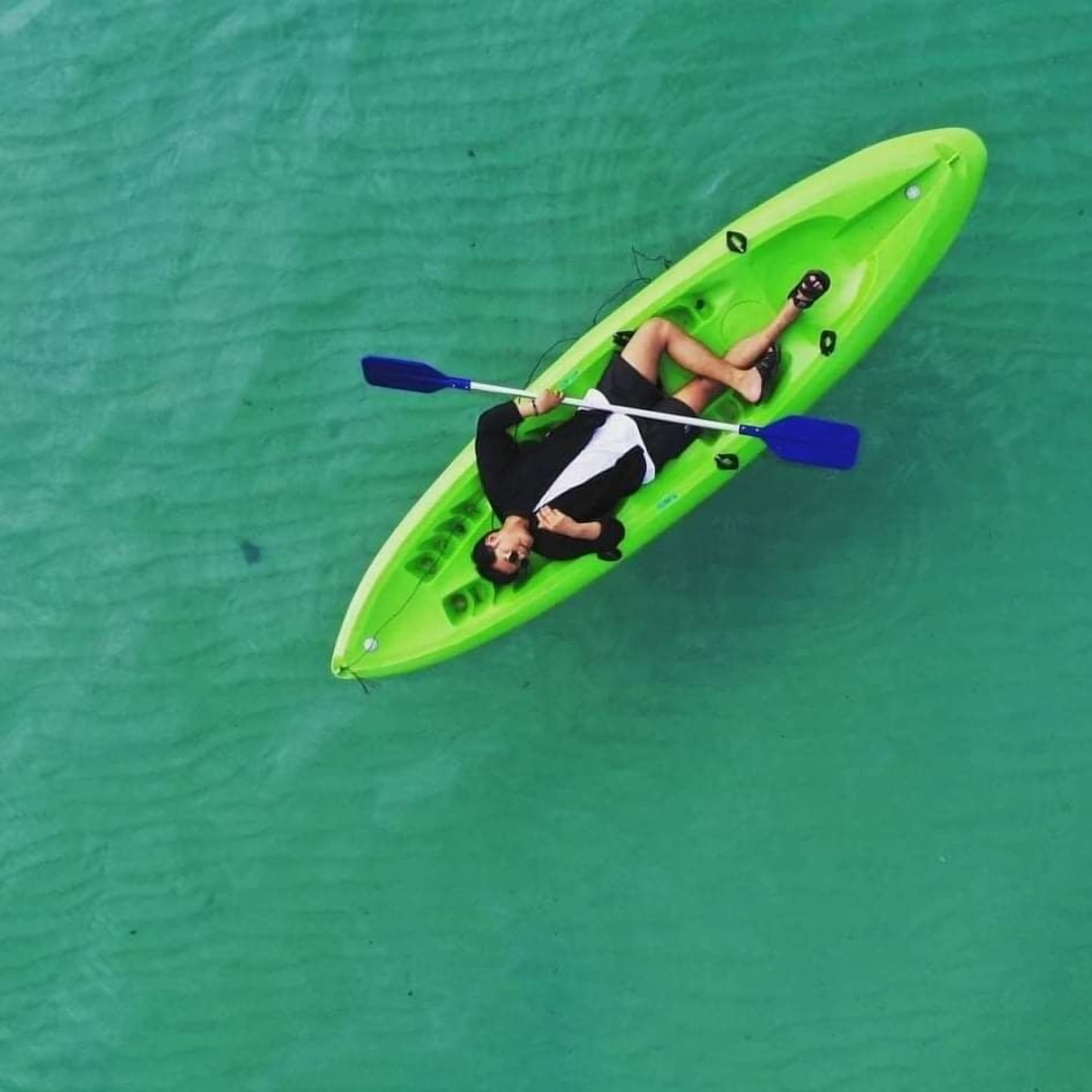Une personne allongée dans un kayak vert sur une étendue d’eau.