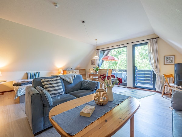 A cozy living room with a sofa, coffee table, and a dining area with chairs and an umbrella.