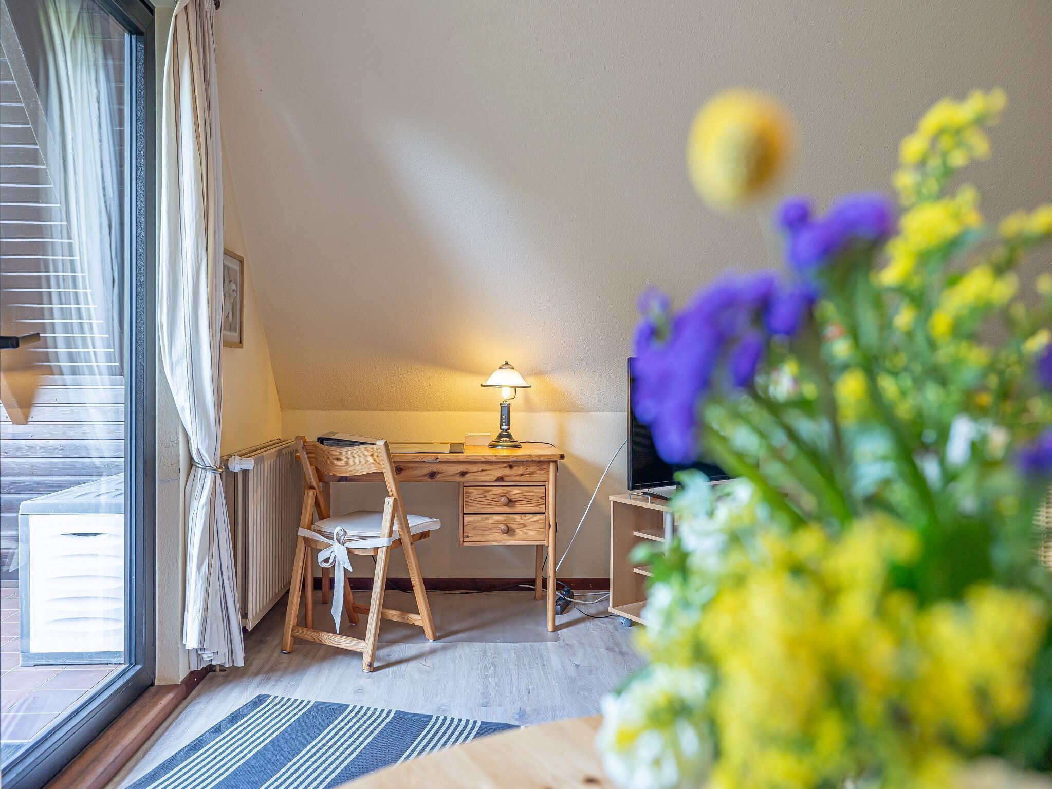 Une pièce confortable avec un bureau en bois, une chaise, une lampe et un téléviseur.