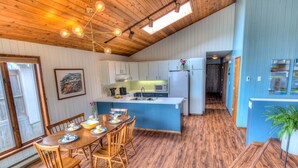 A modern kitchen with wooden flooring, a central island, and a dining area with wooden chairs.