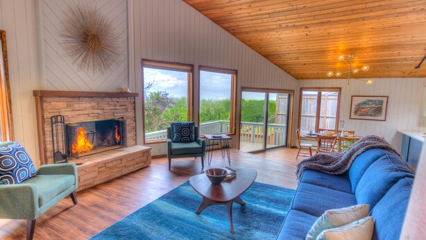 A spacious living room with a fireplace, a large sofa, a dining area, and a view of the outdoors.