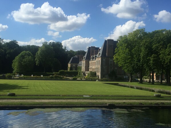 A large, historic building with a symmetrical facade, surrounded by well-manicured lawns and a calm water feature in the foreground.
