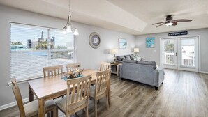 A spacious living area with a dining table, grey sofa, and a ceiling fan.