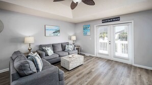A living room with a gray sofa set, a woven coffee table, and a ceiling fan.
