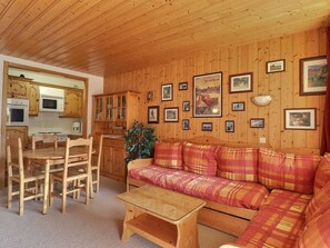 A cozy cabin interior with wooden walls, a dining area with a table and chairs, a sofa, and a kitchen with wooden cabinets and appliances.