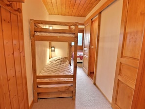 A wooden bunk bed in a hallway with a carpeted floor and wooden walls.