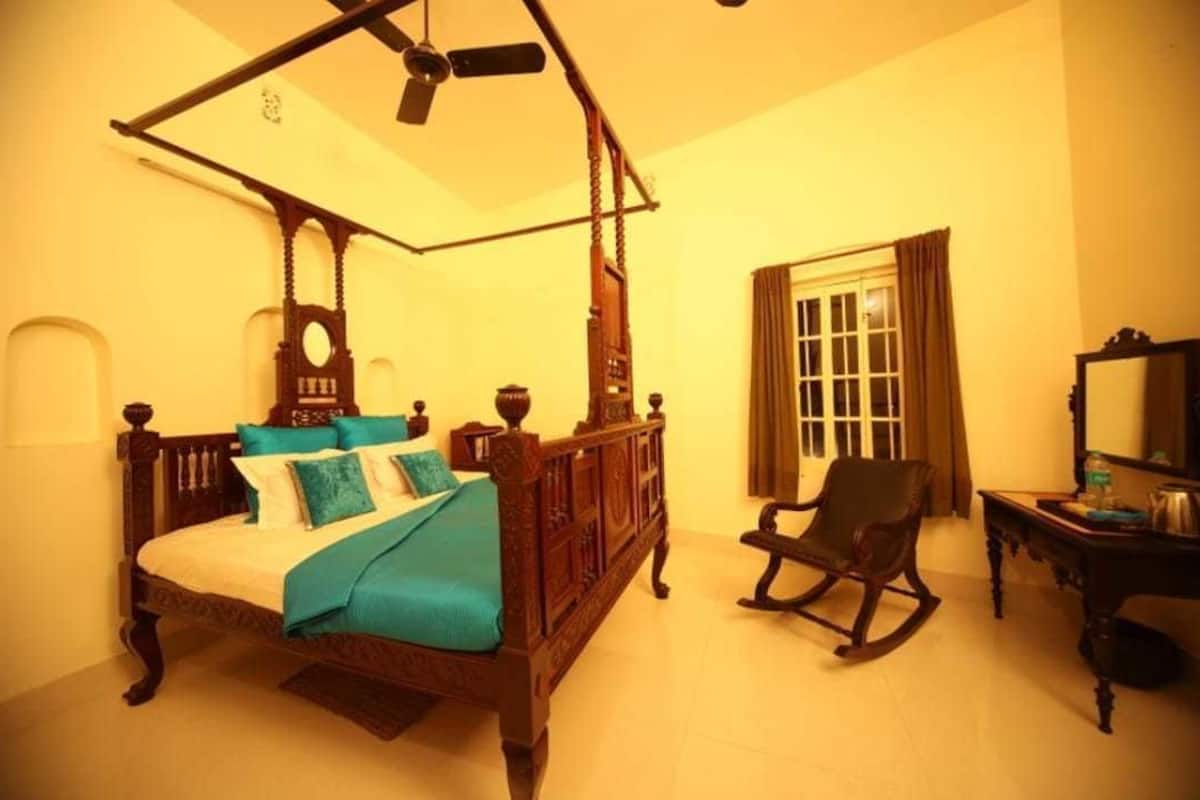 A traditional four-poster bed with a canopy, a rocking chair, and a small table with a mirror.
