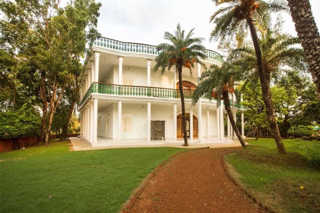 A large, white colonial-style building with a central courtyard, surrounded by lush greenery and palm trees.