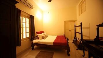A bedroom with a bed, a wooden wardrobe, a piano, and a ceiling fan.