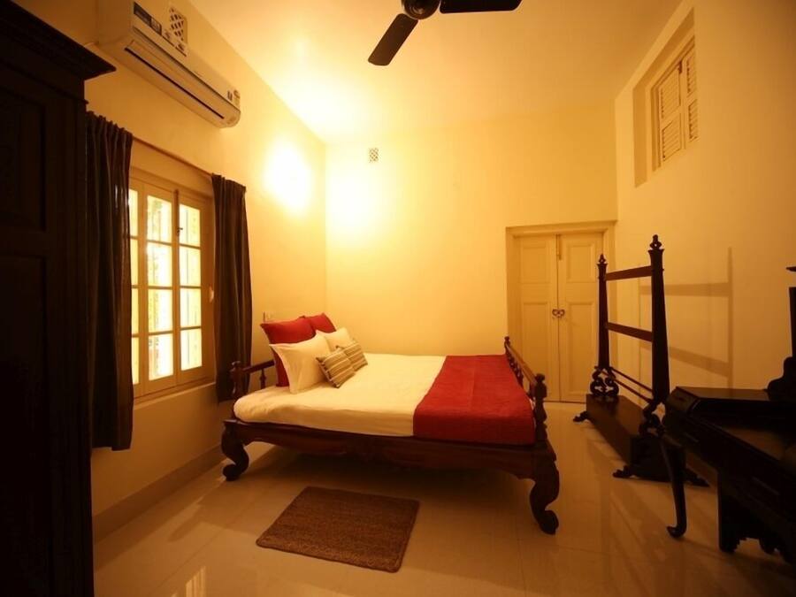 A bedroom with a bed, a wooden wardrobe, a piano, and a ceiling fan.