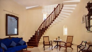 A spacious living room with a wooden staircase, a blue sofa, and two wooden chairs.