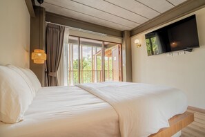 A bedroom with a bed, a television mounted on the wall, and a window with curtains. - Baanna Place (Ban Na)