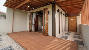 A wooden deck with a door leading to a room, a small outdoor area with gravel, and a wall-mounted sign.