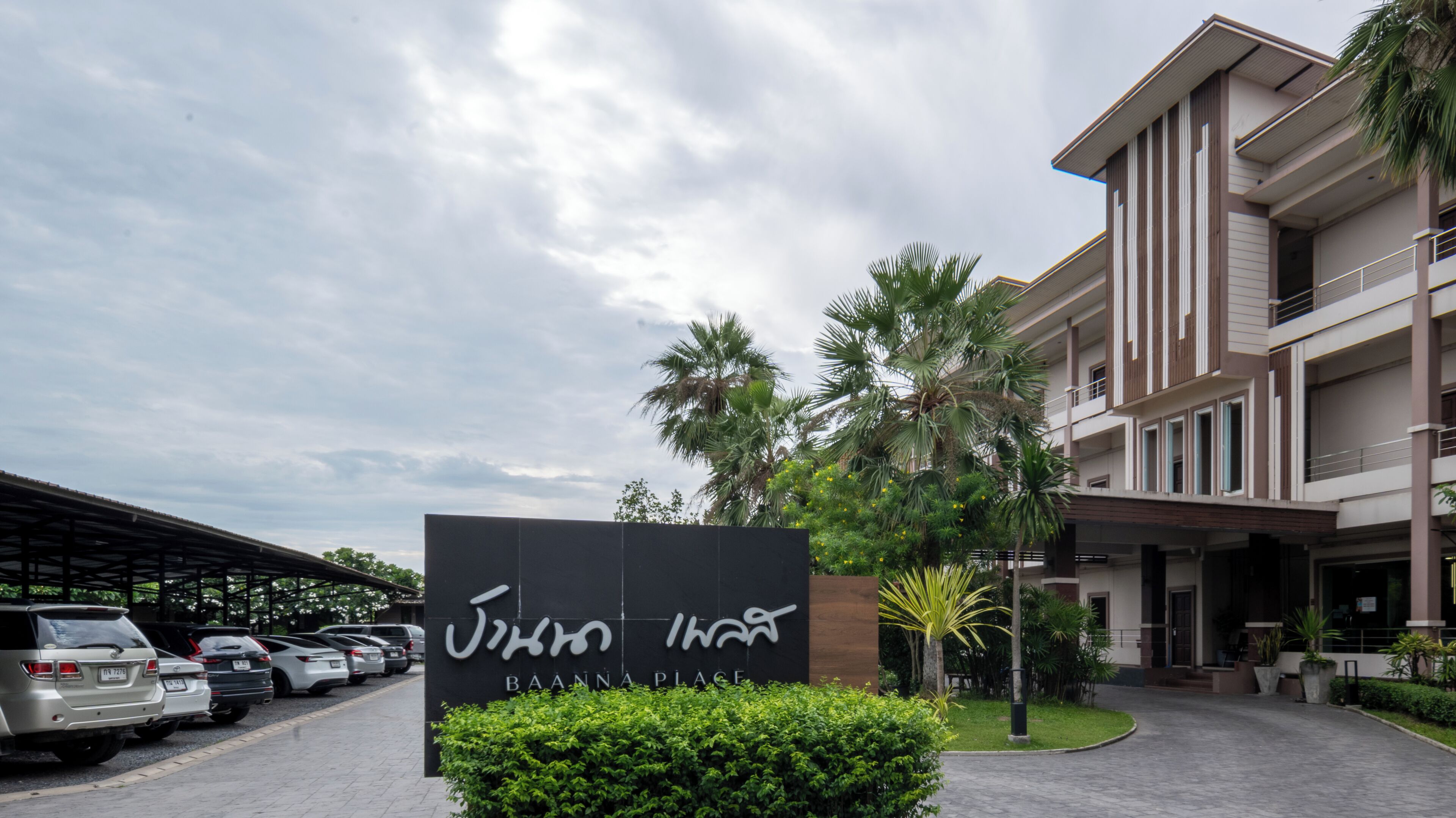A hotel entrance with a sign, parked cars, and a covered parking area.