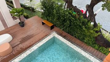 Una piscina en la azotea con terraza de madera, un banco y una pequeña planta en maceta.