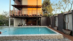 A modern two-story house with a swimming pool, a covered outdoor area, and a staircase leading to a balcony.
