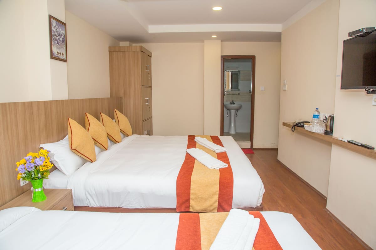 Habitación de hotel con dos camas, un armario de madera, televisión y baño a la vista a través de una puerta abierta.