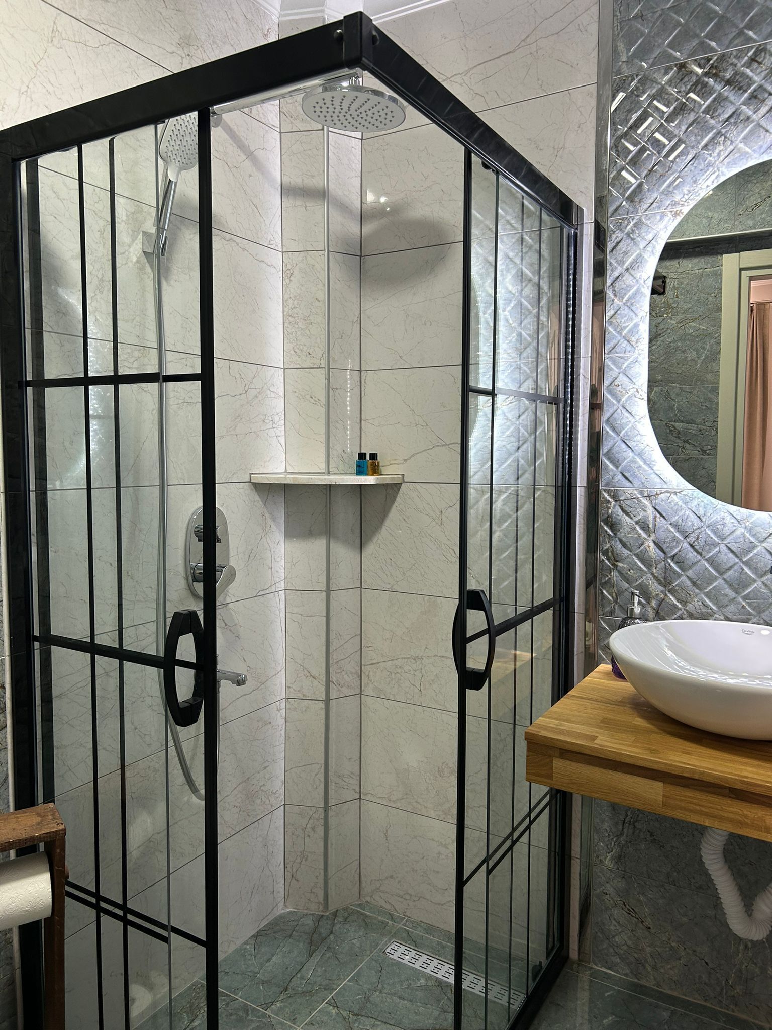 A bathroom with a glass-enclosed shower, a wooden vanity with a sink, and a marble-tiled floor.