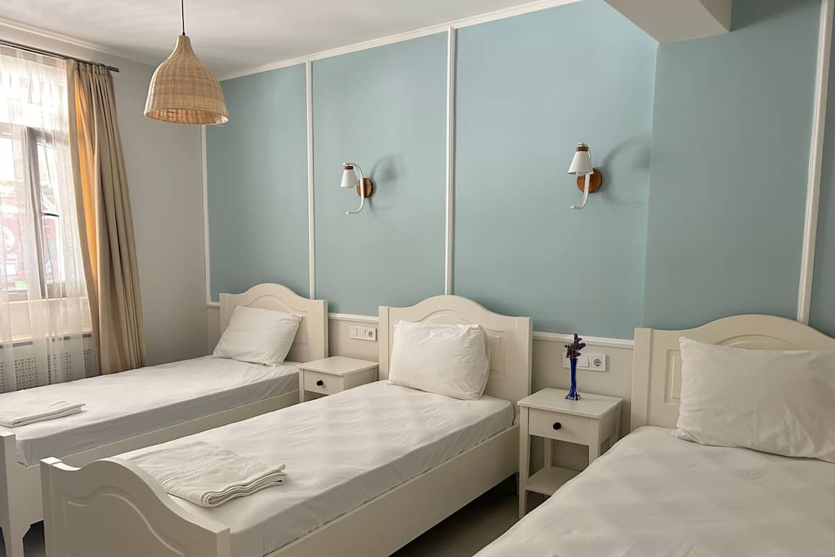Habitación de hotel con dos camas individuales, una mesita de noche con lámpara y una ventana con cortinas.