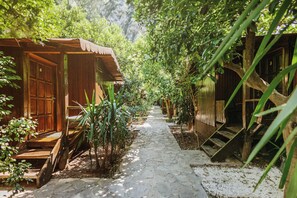 A pathway leading to wooden structures with doors and windows, surrounded by greenery. - Base Bungalows (Kumluca)