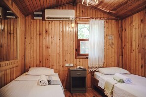 A wooden cabin room with two beds, a nightstand, and an air conditioning unit.